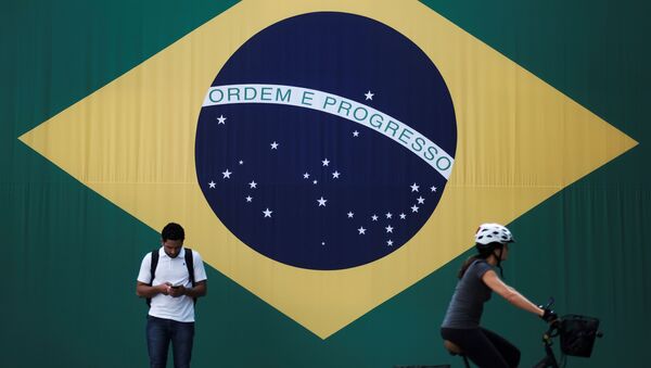 A man checks his mobile phone as a woman riding a bike passes next to a big Brazilian flag in Sao Paulo, Brazil June 28, 2018 - Sputnik International