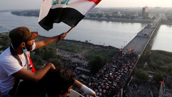 A demonstrator holds an Iraqi flag as he sits on a building during an anti-government protests in Baghdad, Iraq October 30, 2019 - Sputnik International