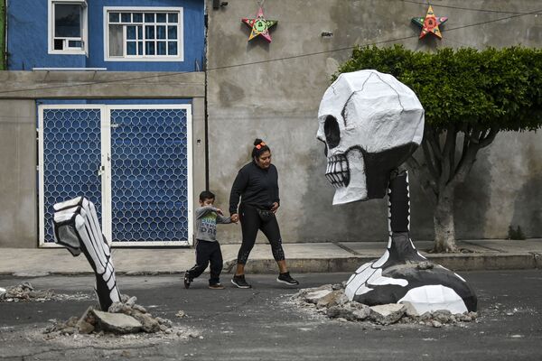 A woman and a child walk next to a huge cardboard skull made by artisans in a street in the Tlahuac neighbourhood, in Mexico City on October 28, 2019, ahead of the Day of the Dead celebrations.  - Sputnik International