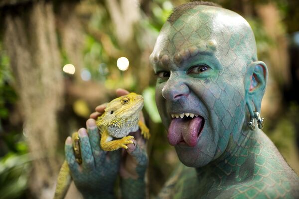 US Erik Sprague, also known as The Lizardman, poses with an iguana. Sprague is a freak show and sideshow performer, known for his body modification, including his sharpened teeth, full-body tattoo of green scales, split tongue, subdermal implants and recently, green-inked lips.   - Sputnik International