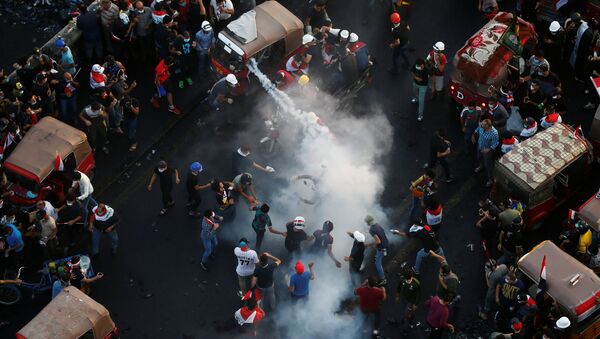 Demonstrators try to put out a tear gas canister during an anti-government protests in Baghdad - Sputnik International