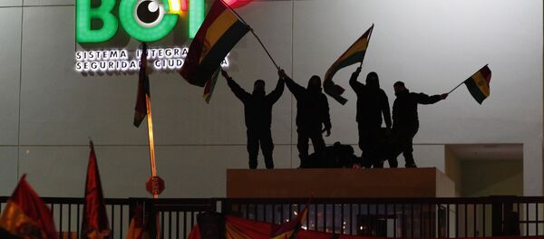 Police officers standing on the rooftop of a security booth at a police station wave Bolivian flags in front of protesters in La Paz Police officers standing on the rooftop of a security booth at a police station wave Bolivian flags in front of protesters in La Paz - Sputnik International
