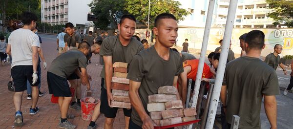 Personnel from the Chinese People's Liberation Army barracks in Hong Kong emerged on to the city streets on November 16, 2019, to help the clean-up after a week of violence and disruption caused by pro-democracy protesters. - In a rare and highly symbolic movement by a garrison which is confined to the barracks under Hong Kong's mini-constitution, scores of men with crewcuts and identical gym kits conducted a lightning-quick removal of bricks and debris near their base. - Sputnik International