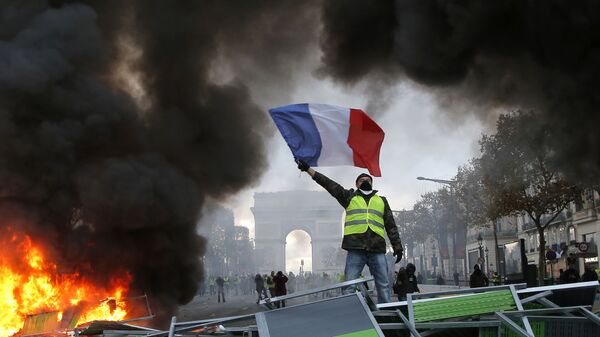 In this Nov. 24, 2018 file photo, a demonstrator waves the French flag on a burning barricade on the Champs-Elysees avenue with the Arc de Triomphe in background, during a demonstration against the rise of fuel taxes.  - Sputnik International