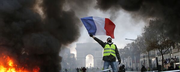 In this Nov. 24, 2018 file photo, a demonstrator waves the French flag on a burning barricade on the Champs-Elysees avenue with the Arc de Triomphe in background, during a demonstration against the rise of fuel taxes.  - Sputnik International
