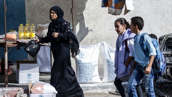 Palestinian pupils walk by a women receiving food aid from a United Nations Relief and Works Agency (UNRWA) distribution centre in the southern Gaza Strip refugee camp of Rafah, on November 17, 2019.  - Sputnik International