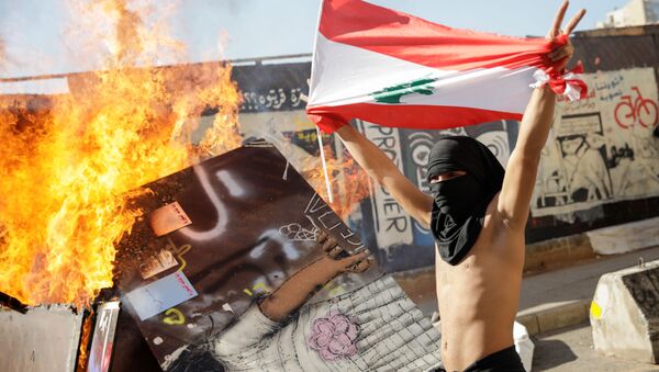 A masked protester holding a Lebanese flag walks past a burning barricade during ongoing anti-government protests in Beirut, Lebanon November 19, 2019 - Sputnik International