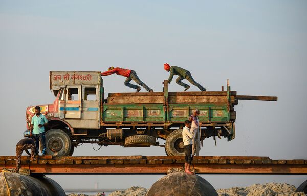 Labourers push wooden boards before carrying them to construct a temporary pontoon bridge over the Ganges River for the upcoming Hindu festival of Magh Mela in Allahabad on 24 November 2019. - Sputnik International