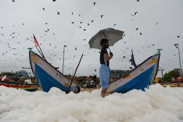 A man looks on as a foamy discharge, caused by pollutants, mixes with surf at Marina beach in Chennai on December 1, 2019.  - Sputnik International