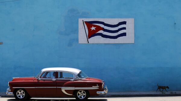 A driver steers his classic car past a wall decorated with a Cuban flag in Havana - Sputnik International