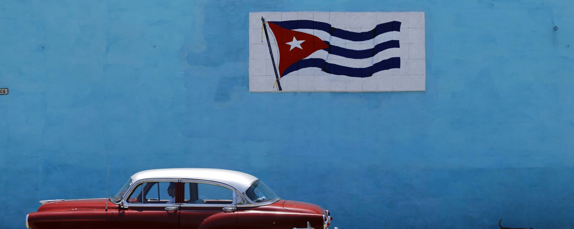 A driver steers his classic car past a wall decorated with a Cuban flag in Havana - Sputnik International, 1920, 03.11.2022
