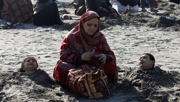 A woman sits near her children, buried up to their necks in sand during a solar eclipse, along Clifton beach in Karachi, Pakistan December 26, 2019 - Sputnik International