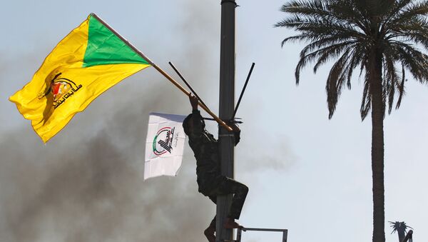 A member of the Hashd al-Shaabi paramilitary forces holds a flag of the Kataib Hezbollah militia group during a protest to condemn air strikes on their bases, in Baghdad, Iraq, 31 December 2019.  - Sputnik International
