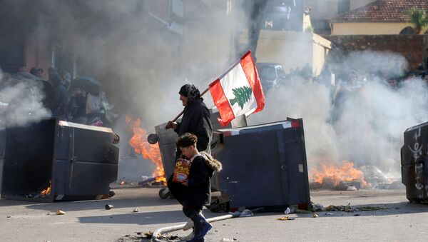A protestor holding the Lebanese flag walks near burning barricades during a protest over economic hardship and lack of a new government in Beirut, Lebanon January 14, 2020.  - Sputnik International