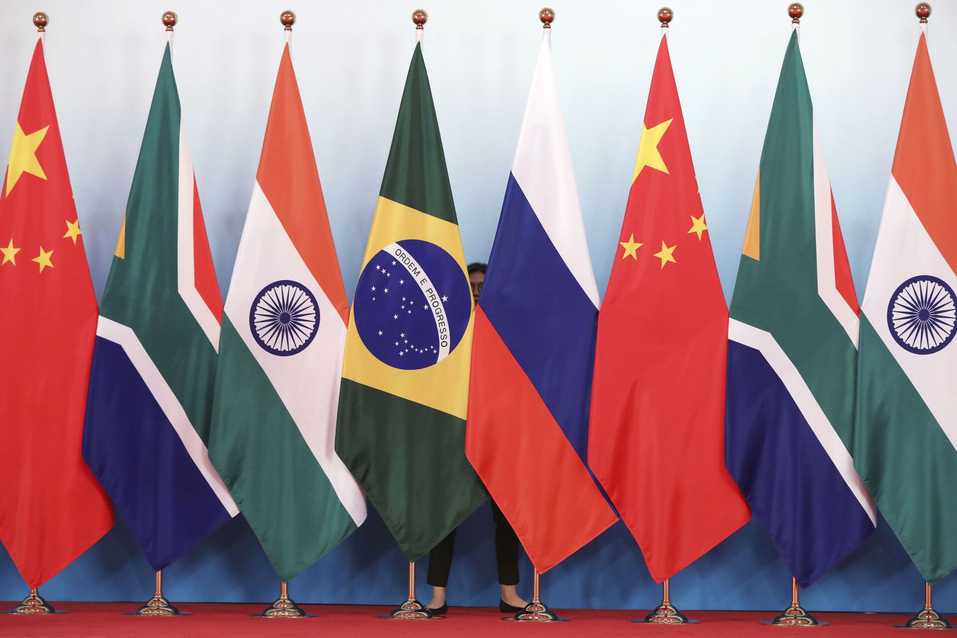 Staff worker stands behinds national flags of Brazil, Russia, China, South Africa and India to tidy the flags ahead of a group photo during the BRICS Summit at the Xiamen International Conference and Exhibition Center in Xiamen, southeastern China's Fujian Province, Monday, Sept. 4, 2017. - Sputnik International, 1920, 27.02.2022