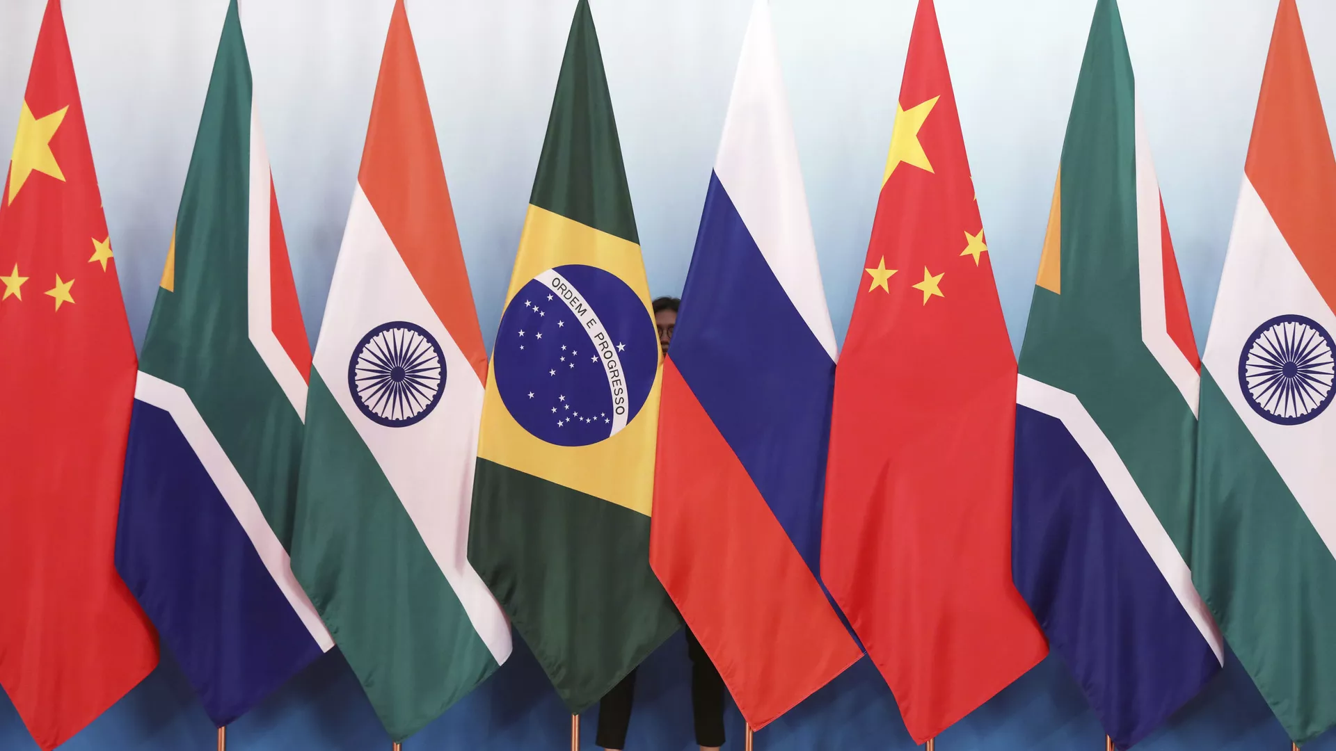 Staff worker stands behinds national flags of Brazil, Russia, China, South Africa and India to tidy the flags ahead of a group photo during the BRICS Summit at the Xiamen International Conference and Exhibition Center in Xiamen, southeastern China's Fujian Province, Monday, Sept. 4, 2017. - Sputnik International, 1920, 29.05.2023