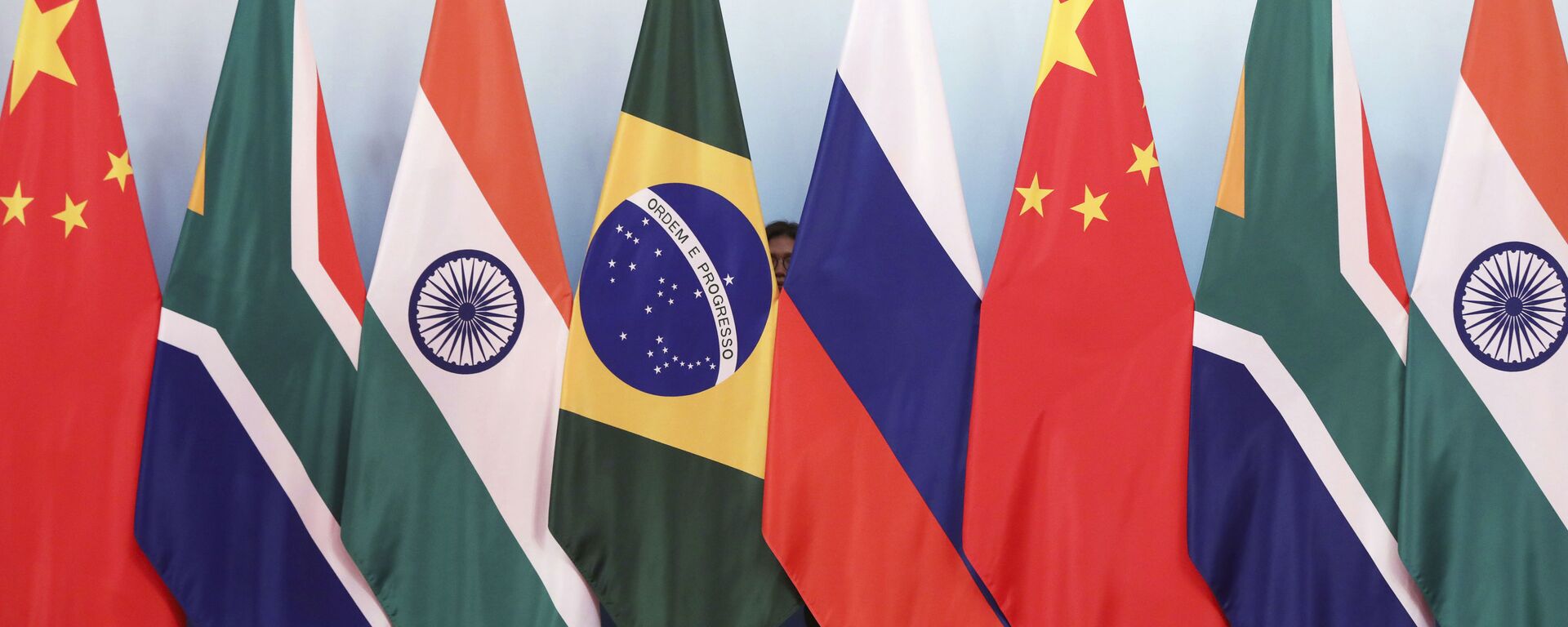 Staff worker stands behinds national flags of Brazil, Russia, China, South Africa and India to tidy the flags ahead of a group photo during the BRICS Summit at the Xiamen International Conference and Exhibition Center in Xiamen, southeastern China's Fujian Province, Monday, Sept. 4, 2017. - Sputnik International, 1920, 15.04.2022