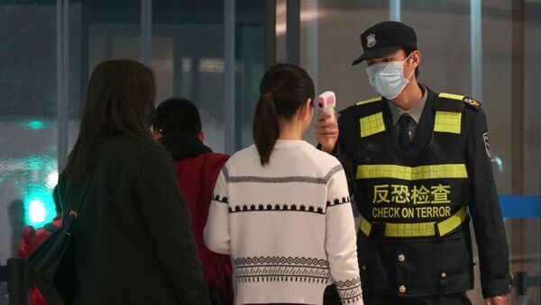 An airport staff member uses a temperature gun to check people leaving Wuhan Tianhe International Airport in Wuhan, China - Sputnik International