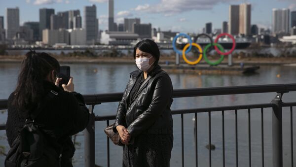 A tourist wearing a mask pauses for photos with the Olympic rings - Sputnik International