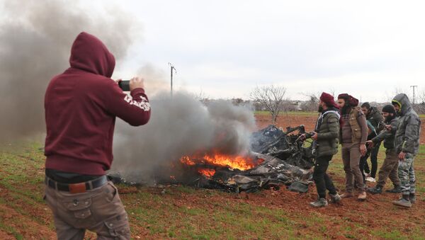 Syrian rebel fighters gather around the burning remains of a military helicopter after it was shot down over the village of Qaminas, about 6 kilometres southeast of Idlib city in northwestern Syria on February 11, 2020 - Sputnik International