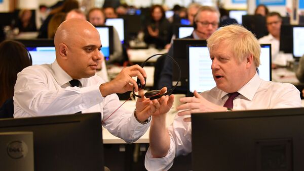 In this file photo taken on December 08, 2019 Britain's Chancellor of the Exchequer Sajid Javid (L) passes a headset to Britain's Prime Minister Boris Johnson (R) so that he can speak to a supporter as they man the phones at the Conservative Campaign Headquarters Call Centre in central London on December 8, 2019.  - Sputnik International