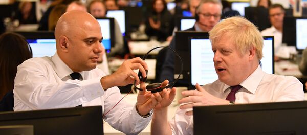 In this file photo taken on December 08, 2019 Britain's Chancellor of the Exchequer Sajid Javid (L) passes a headset to Britain's Prime Minister Boris Johnson (R) so that he can speak to a supporter as they man the phones at the Conservative Campaign Headquarters Call Centre in central London on December 8, 2019.  - Sputnik International