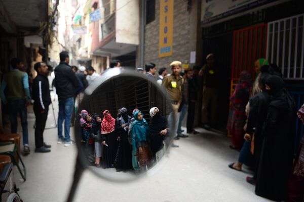 Voters are seen reflected on a mirror as they queue at a polling station to cast their votes during the Legislative Assembly elections in New Delhi on February 8, 2020.  - Sputnik International