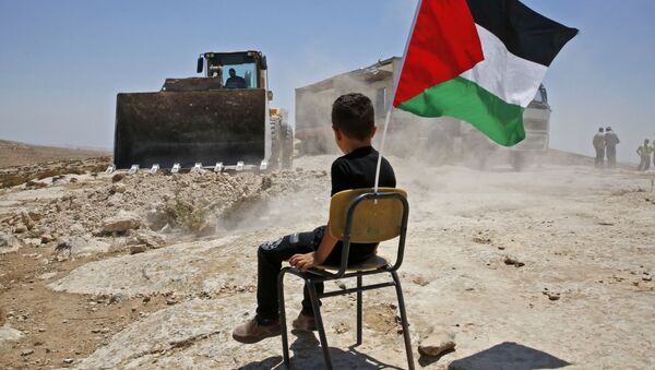 A Palestinian boy sits on a chair with a national flag as Israeli authorities demolish a school site in the village of Yatta, south of the West Bank city of Hebron and to be relocated in another area, on July 11 2018.  - Sputnik International