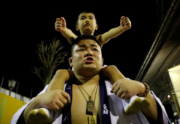 A man carries a boy on his shoulders during a naked festival where men dressed in loincloths try to snatch a wooden stick  - Sputnik International