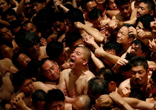 Men dressed in loincloths react as a priest splashes water on them before they prepare to snatch a wooden stick - Sputnik International
