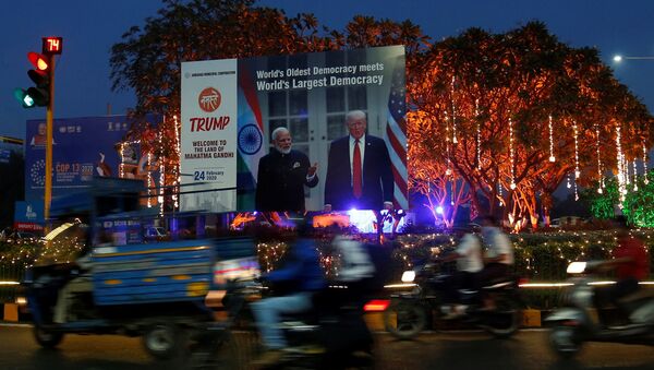 People ride their motorbikes past a hoarding with the images of India's Prime Minister Narendra Modi and U.S. President Donald Trump installed next to decorated trees alongside a road ahead of Trump's visit, in Ahmedabad, India, February 20, 2020 - Sputnik International