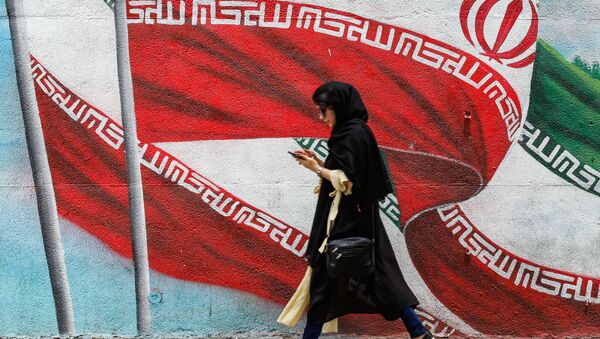 A woman uses her phone as she walks past a mural depicting flying Iranian national flags along a street in the Iranian capital Tehran on July 22, 2019 - Sputnik International