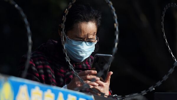 FILE PHOTO: A woman uses her mobile phone behind barbed wire at an entrance of a residential compound in Wuhan - Sputnik International