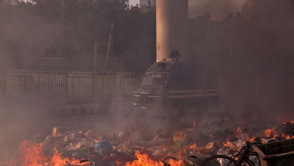 A police vehicle moves past burning debris that was set on fire by demonstrators in a riot affected area after fresh clashes erupted between people demonstrating for and against a new citizenship law in New Delhi, India, February 25, 2020. - Sputnik International