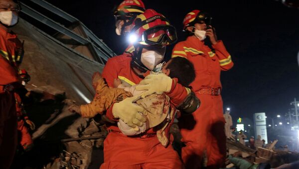 A worker wearing a face mask rescues a child at the site where a hotel being used for the coronavirus quarantine collapsed, in the southeast Chinese port city of Quanzhou, Fujian province, China March 8, 2020 - Sputnik International