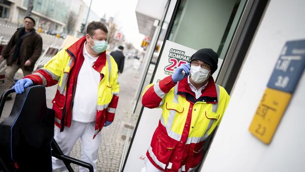 Paramedics from a patient transport company wearing face masks and gloves as they stand at the entrance to an apartment building to pick up a patient in the district Steglitz in Berlin, Germany, March 17, 2020 - Sputnik International