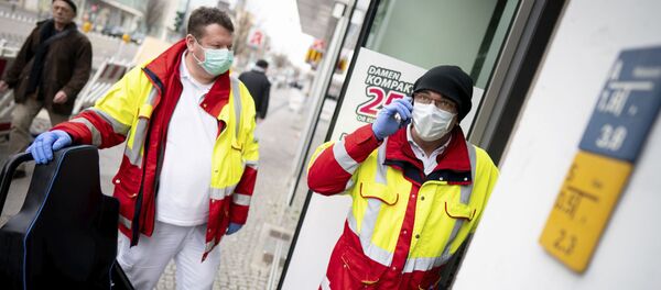 Paramedics from a patient transport company wearing face masks and gloves as they stand at the entrance to an apartment building to pick up a patient in the district Steglitz in Berlin, Germany, March 17, 2020 - Sputnik International