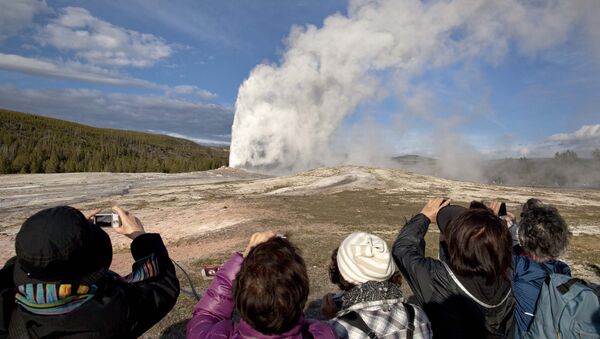 In this May 21, 2011 file photo, tourists photograph Old Faithful erupting, at Yellowstone National Park, in Mont. Old Faithful is among the park’s hydrothermal features powered by the Yellowstone supervolcano. Scientists have discovered a new, deeper reservoir of partly molten rock beneath the Yellowstone supervolcano. But they said the find doesn’t change the chances of a volcanic eruption.  - Sputnik International