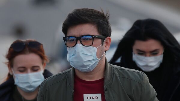 People wearing protective masks walk near a hospital for patients infected with coronavirus disease (COVID-19) on the outskirts of Moscow, Russia March 23, 2020. - Sputnik International