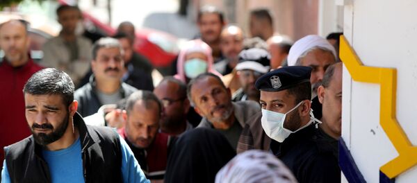 A policeman, wearing a mask as a precaution against the the coronavirus disease (COVID-19), stands guard as Palestinians wait outside a bank to withdraw cash, in Gaza City 29 March 2020. - Sputnik International