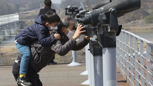 Дедушка с внуком в медицинских масках смотрят в бинокль в городе Паджу на границе с Северной Кореей - Sputnik International