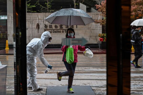 A hotel employee wearing a protective suit sprays disinfectant on an arriving guest, as a preventative measure against the COVID-19 coronavirus in Wuhan, China's central Hubei province on March 29, 2020, a day after travel restrictions into the city were eased following the outbreak - Sputnik International