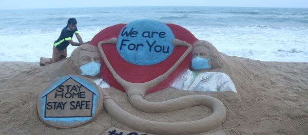 Indian artist Sudarsan Pattnaik puts some final touches as he makes a sand sculpture depicting doctors wearing protective facemasks with a message reading We are For You, Stay Home Stay Safe at Puri beach in Puri on April 3, 2020.  - Sputnik International