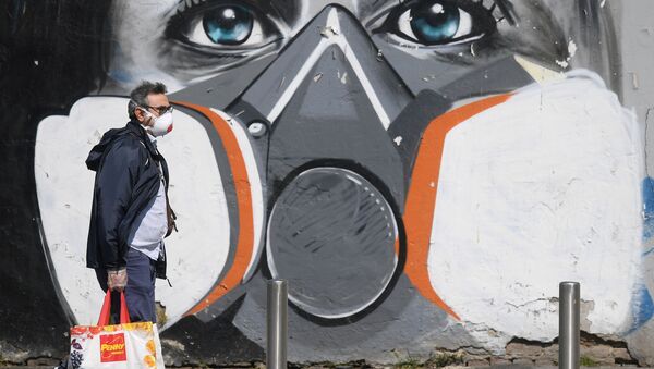 A man wearing a face mask walks past a graffiti - Sputnik International