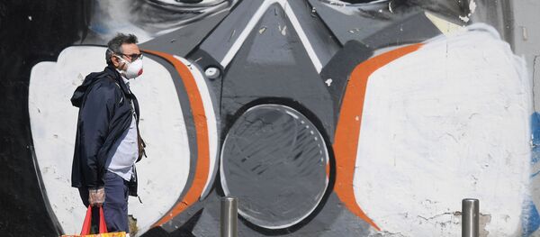 A man wearing a face mask walks past a graffiti - Sputnik International