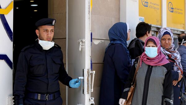 A Palestinian policeman stands guard as a woman, wearing a mask as a precaution against the the coronavirus disease (COVID-19), waits with other people outside a bank to withdraw cash, in Gaza City March 29, 2020 - Sputnik International