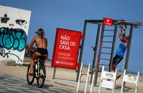 A woman riding a bicycle passes a sign which reads Don't leave the house at Ipanema beach, during the coronavirus disease (COVID-19) outbreak, in Rio de Janeiro, Brazil April 5, 2020.  - Sputnik International