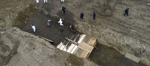 Workers wearing personal protective equipment bury bodies in a trench on Hart Island, Thursday, April 9, 2020, in the Bronx borough of New York. On Thursday, New York City’s medical examiner confirmed that the city has shortened the amount of time it will hold on to remains to 14 days from 30 days before they will be transferred for temporary internment at a City Cemetery. Earlier in the week, Mayor Bill DeBlasio said that officials have explored the possibility of temporary burials on Hart Island, a strip of land in Long Island Sound that has long served as the city’s potter’s field. - Sputnik International