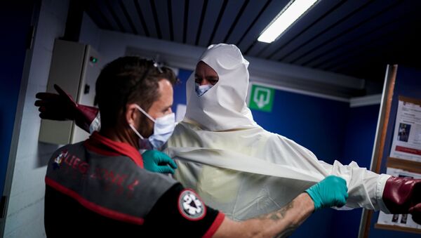 A Belgian fireman is helped into a personal protective equipment (PPE) kit before disinfecting an ambulance at the Central Fire Station in Liege on April 10, 2020 - Sputnik International