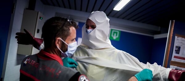 A Belgian fireman is helped into a personal protective equipment (PPE) kit before disinfecting an ambulance at the Central Fire Station in Liege on April 10, 2020 - Sputnik International